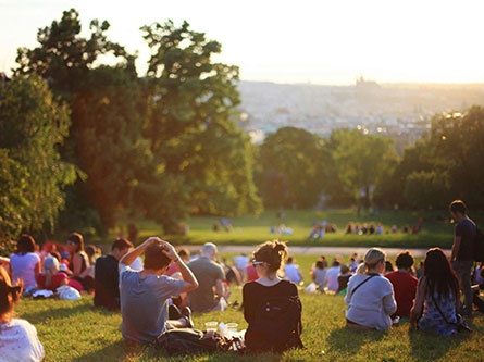 Dozens of people sitting on a grassy hillside overlooking a city sunset