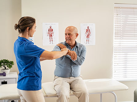 older man pointing to his shoulder pain with health care provider ahead of shoulder replacement surgery