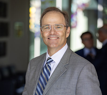 Dr. Joshua Fenton in a white shirt and grey jacket smiling to the camera.