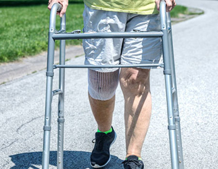 Lower extremity of person walking with the assistance of a walker who has their right knee covered in bandage.