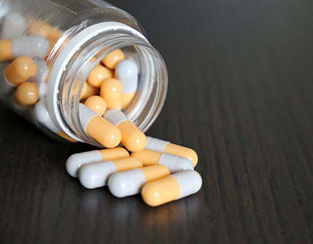 A medicine bottle lays on its side, as yellow and white pill capsules spill out.