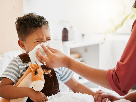 A boy holding a stuffed animal whle his mother holds a tissue to his nose