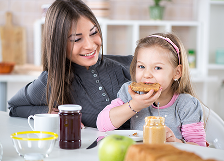 Mom watching young daughter eat bread and peanut butter