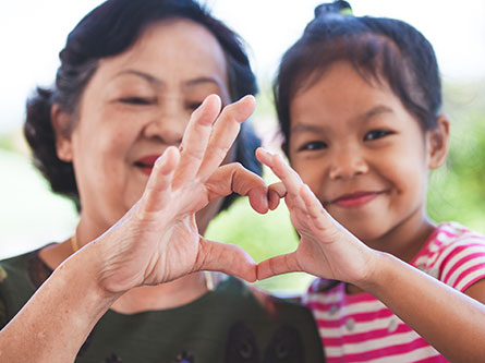 older woman and young girl making a heart with their hands