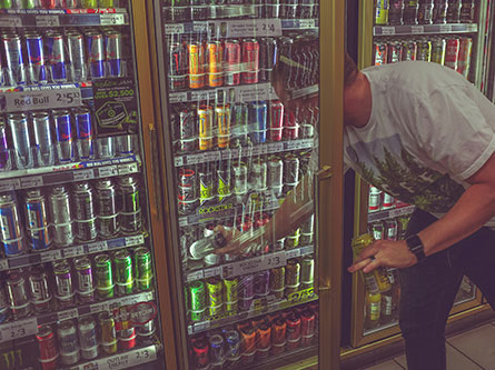 man reaching for energy drinks in a store refrigerator