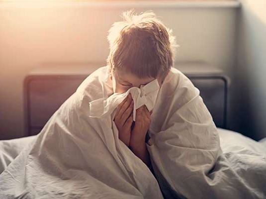 kid in bed blowing nose