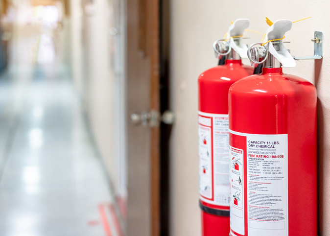 Two fire extinguishers hanging on the wall of a public hallway.